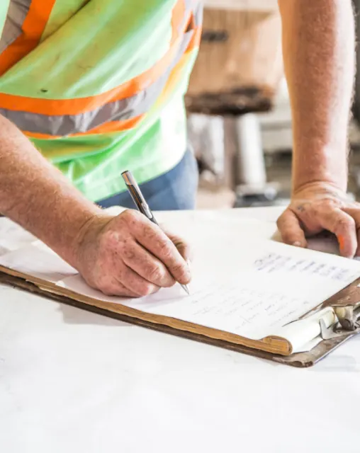 Worker in a high-visibility vest completing paperwork on a clipboard