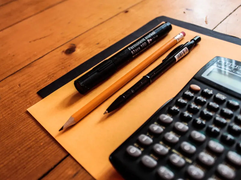 Calculator and pens resting on an envelope on a wooden desk